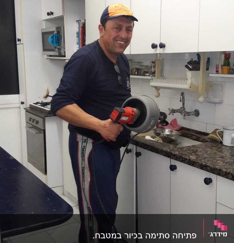 אדם מחזיק מכשיר אינסטלציה ליד כיור מטבח